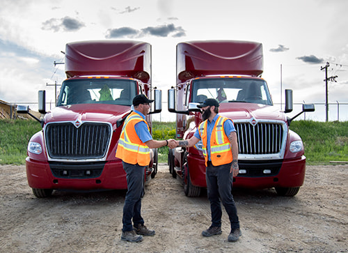 two men wearing safety vest in front of two red semi-trucks