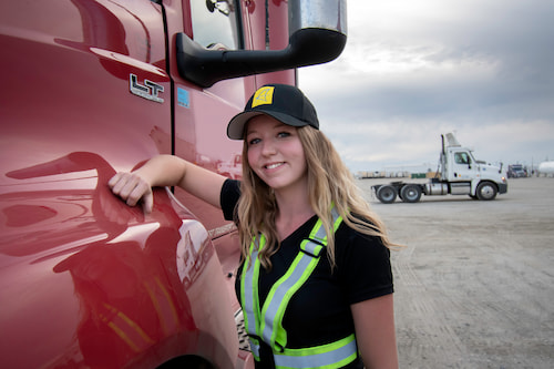 female wearing a safety strap and Tag Logistics hat leaning on a red semi-truck